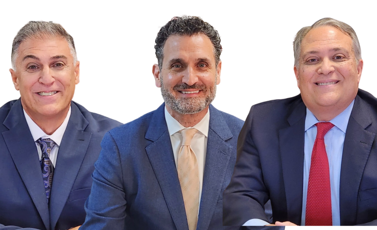 Three men in business suits sit side by side, smiling at the camera against a plain white background. The man in the center has a beard, while the men on either side are clean-shaven.